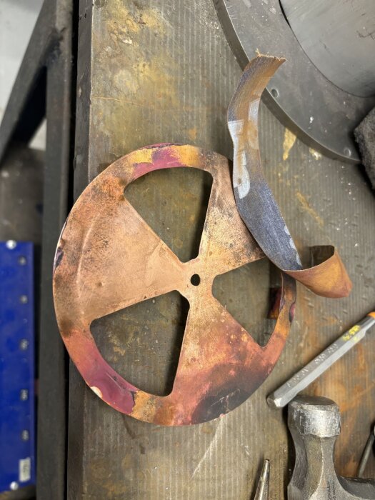 Rund kopparskiva med utskurna sektioner, verktyg vid sidan på ett arbetsbord, del av hemgjord bastuventil.