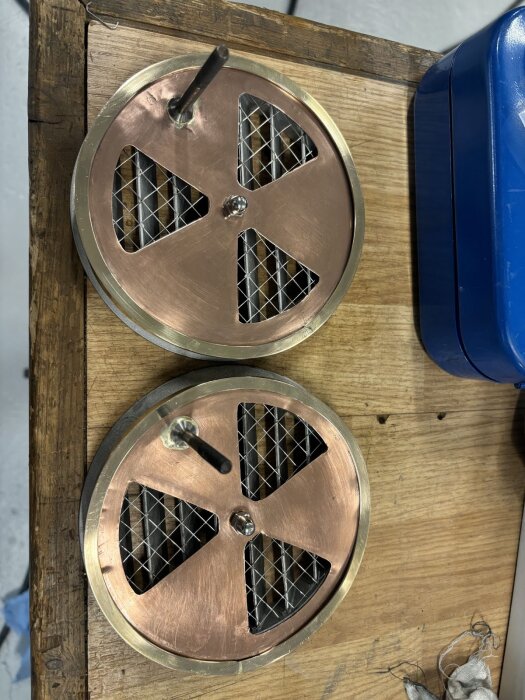 Två kopparventiler med nät och skruvhandtag monterade på en träyta, del av bastuventilationsprojekt.