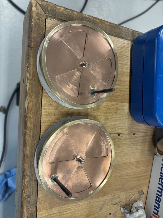 Två runda kopparventiler med skruvhandtag och mässingskant, liggande på ett träbord.