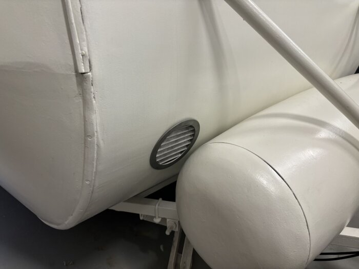 Vit discoventil monterad på utsidan av en bastuvagn i aluminium, med en diskret och stilren design vid vagnens nederkant.