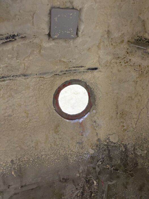 Rund ventilationsöppning i en isolerad vägg, omgiven av applicerat tätningsmedel, med genomkik till dagsljus.