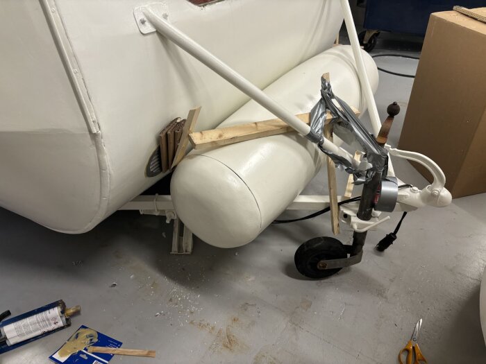 Vitmålad släpvagn med monterade ventilationsventiler och provisorisk fastsättning med trä och silvertejp i ett garage. Verktyg och material på golvet.