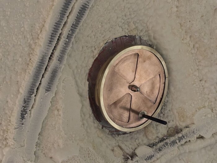 Ventilationsventil i koppar med en mässingsram, monterad på en beige yta med textur, synligt handtag för manuell justering.