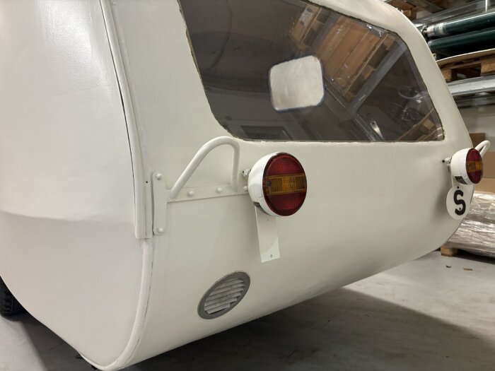 Vit vagn med ventilationsgaller och bakljus, fotograferad bakifrån.