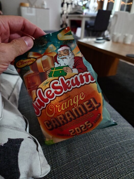 En hand håller en påse med "Juleskum Orange Caramel" från Cloetta, med en tecknad tomte och karamellmotiv på förpackningen.
