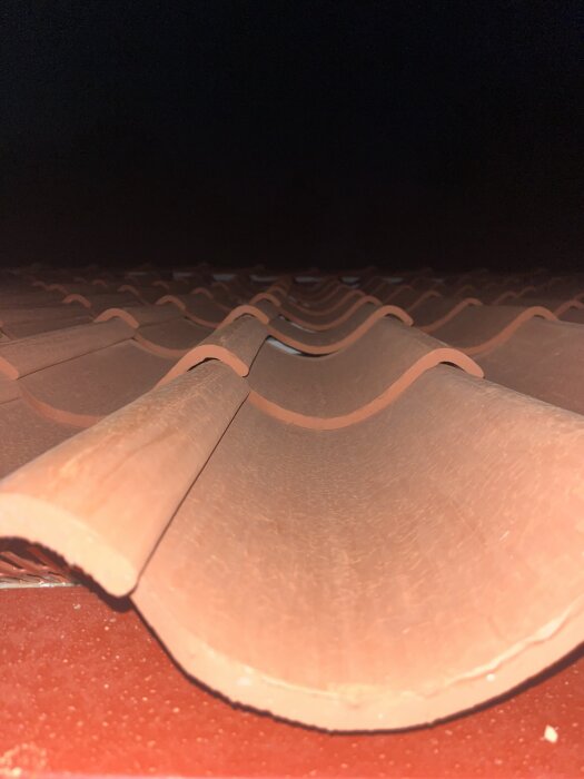 Enkupiga tegelpannor på tak med glipor mellan rader, fotade i mörkret.