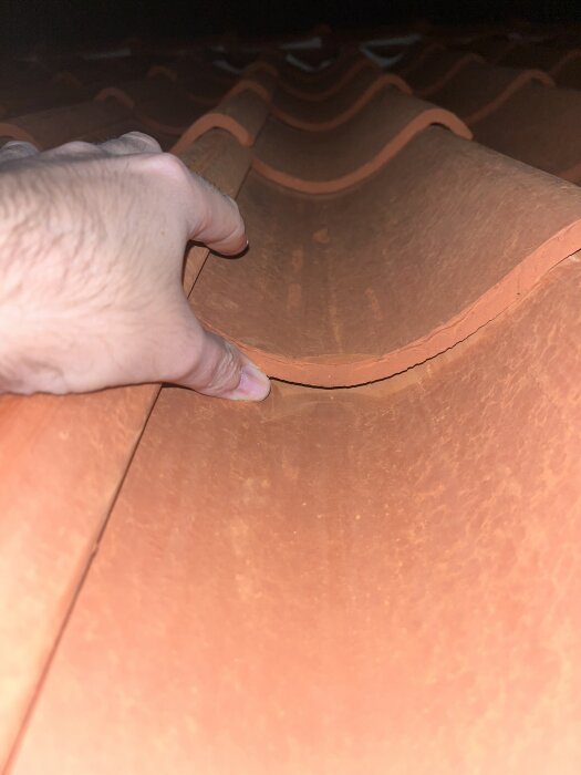Hand undersöker fingerstor glipa mellan enkupiga tegelpannor på tak.