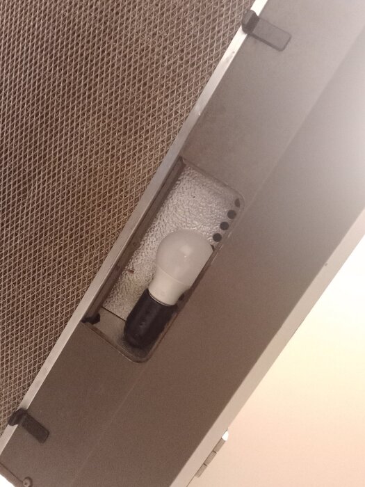 Glödlampa monterad i en köksfläkt, synlig från undersidan.