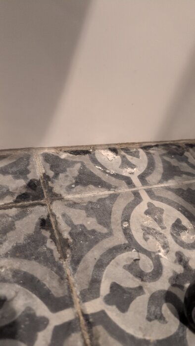 Sprucken list och fläckiga golvfogar på mönstrat kakel i villa med gjuten platta. Eventuell läcka från duschbrunn.