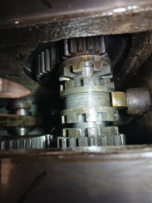 Närbild av ett maskineri med synliga kugghjul, troligen en mekanism som kräver kvarhållande spak, där något verkar saknas för korrekt funktion.