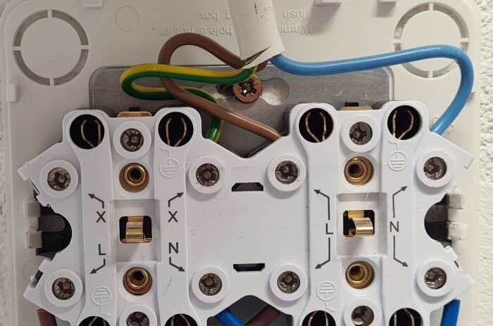 Närbild av ett vägguttag med inkommande jord ansluten till fel plint och felaktig kabeldragning.