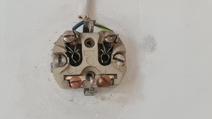 Föråldrat eluttag utan korrekt jordanslutning, visar blottade ledare och osäker installation på rått betonggolv i en källare.