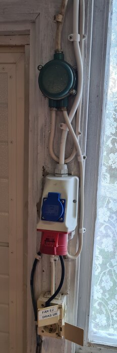 Elektriska uttag och kablar på vägg, med ett synligt trefasuttag och en varningsskylt som säger "FÅR EJ DRAS UR".