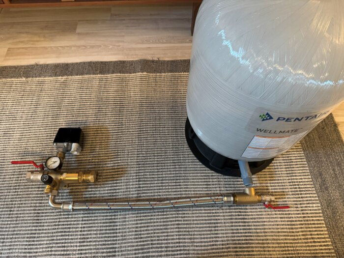 Bild på en Pentair Wellmate membranhydrofor bredvid tryckregleringsdelar på en matta.