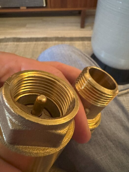 Närbild av två guldglänsande metalldelar med rörgängor som hålls av en hand; delarna ska kopplas ihop i ett hydropressystem.