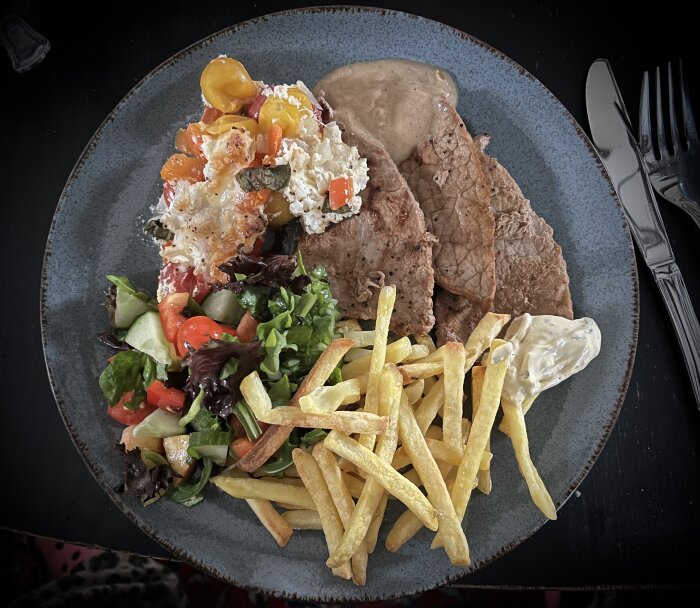 Tallrik med lövbiff, pommes frites, bearnaisesås, sallad och bakad tomat- och paprikaröra med burrata.