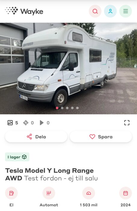 Husbil parkerad utanför ett garage, vit med hymer logotyp, vid blöt asfaltsyta, omgiven av grönska.