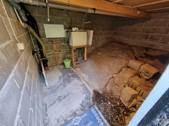 Källarutrymme under hus med blottad berggrund, vattenrör, vattenmätare och löst placerade element för frostskydd.