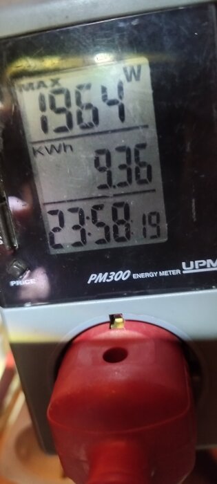 Närbild av en energimätare som visar max 1964 W, totalt 9.36 kWh, med text PM300 Energy Meter och del av röd kontakt.