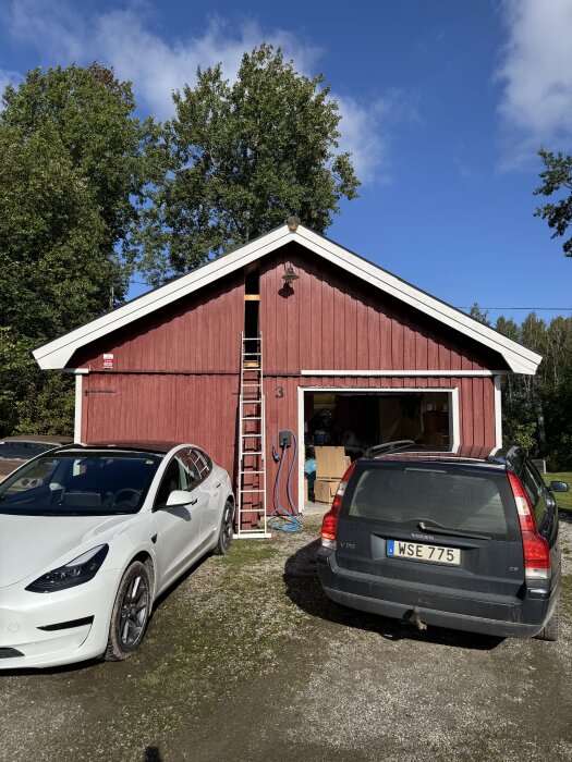 Rött garage med förråd och carport, två bilar framför, stege vid gaveln, plan ska skapa dubbelgarage, fråga om takstolar.