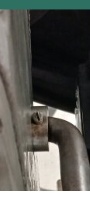 En närbild på en skruvad spårskruv fäst i en böjd metallstång eller rör, intill en annan metallisk yta.