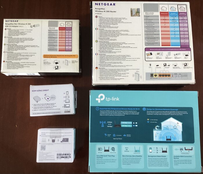 Kartonger med nätverksutrustning på ett bord, inklusive Netgear och TP-Link produkter, diskuteras för användning som signalförstärkare i ett gårdshus.