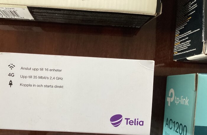Närbild av en vit Telia-produktlåda med text om 4G-anslutning och möjligheten att koppla upp till 16 enheter, samt TP-Link AC1200-låda.