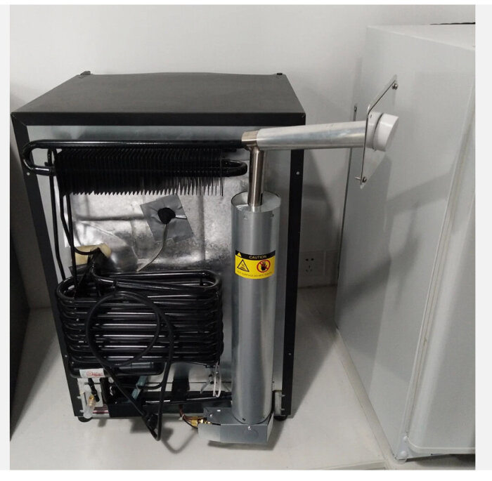 En tillbehörssats med värmetålig slang och genomföring för att leda avgaser genom en vägg, monterad på en liten metallbox.