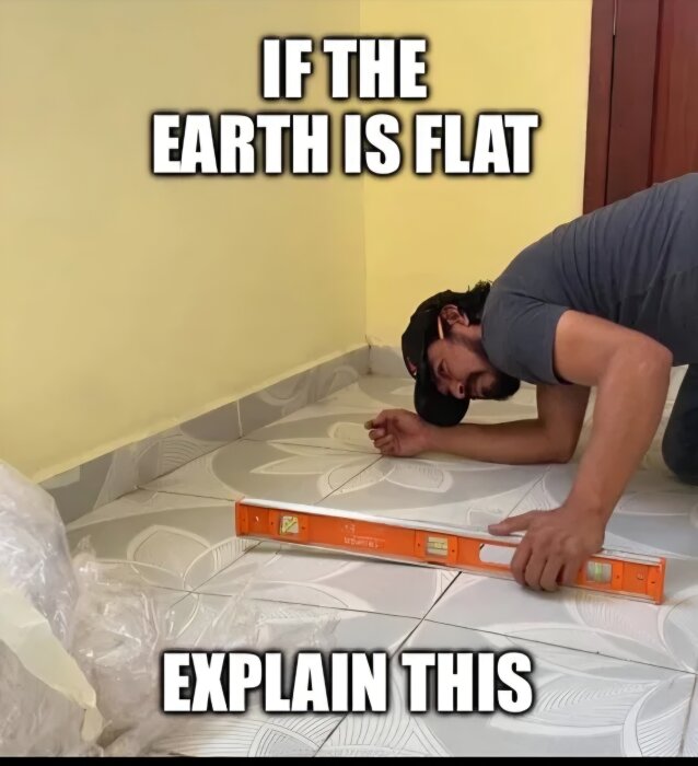 En person använder ett vattenpass mot golvet bredvid en vägg med texten "If the earth is flat, explain this".