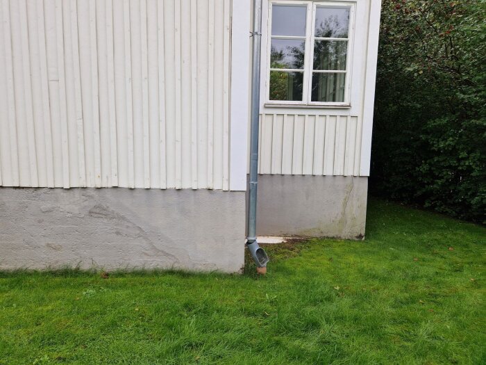 Husgrund med sprickor och brädfodrad fasad, stuprör syns och det är grön gräsmatta runt omkring.