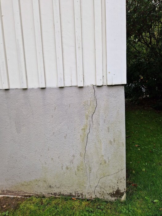 Spricka i fasadens sockel av ett hus, visar tecken på tidigare lagningar och fortsatt rörelse. Gräsmatta i förgrunden.