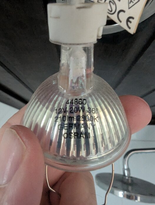 Takspotlight av märket Osram, 12V 20W, visas i närbild med etikettinformation, hålls i handen över en takarmatur.