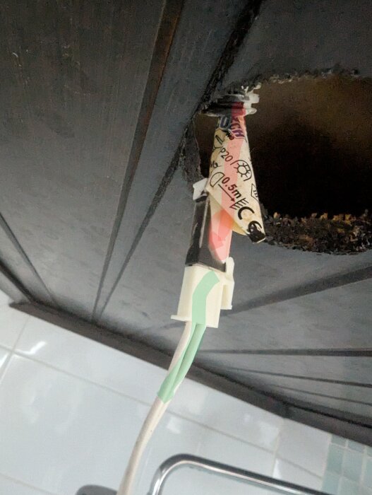 Bränd kabel och koppling under ett tak, med en röd märkning som visar skadad kabel efter strömspik i badrumsbelysning.