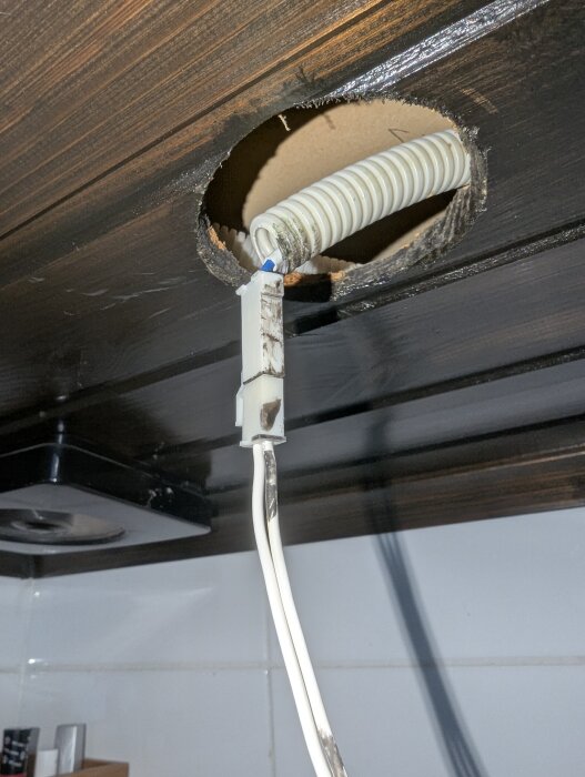 Bränd kabelkoppling och skyddsslang i tak med trasig spottbelysning, exponerad under reparation efter strömspik i badrummet.