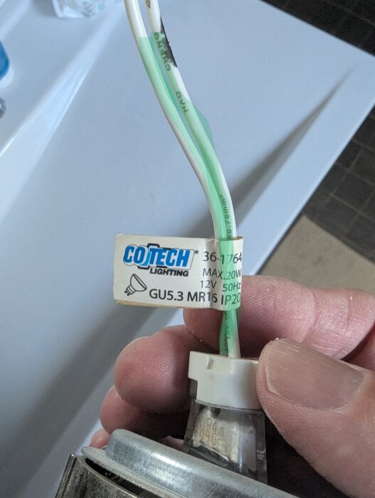 Hand som håller en takspot med vit och grön kabel och etikett från Cotech Lighting med specifikationer för lampan.