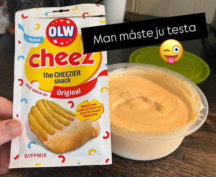 Förpackning med OLW Cheez dippmix och en skål med färdig dippsås på ett mörkt bord. Text medför ett humoristiskt emoji.