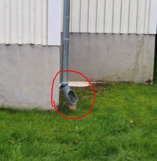 Takränna vid husvägg med tydlig rörelse i marken kring avloppsrör, omgiven av grön gräsmatta och murad fasad.