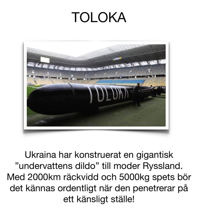En stor svart torpedliknande föremål med texten "TOLOKA" på sidan visas i en stadionmiljö.