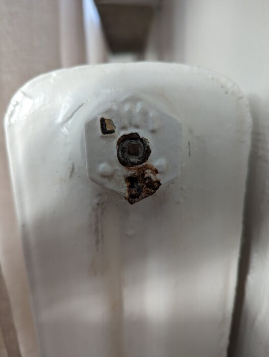 Rostig ventil med läckage på ett vitt element, fokus på en stor mutter med rost runt om.