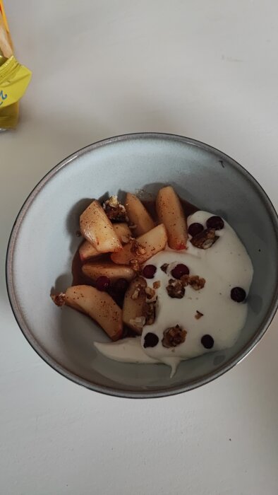 Skål med smör- och honungsstekta äppelklyftor, vaniljkräm, hasselnötsknäcke, kanel och lingon.