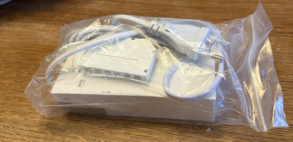 Vit LED-driver med grenuttag ligger i en plastpåse på ett bord.