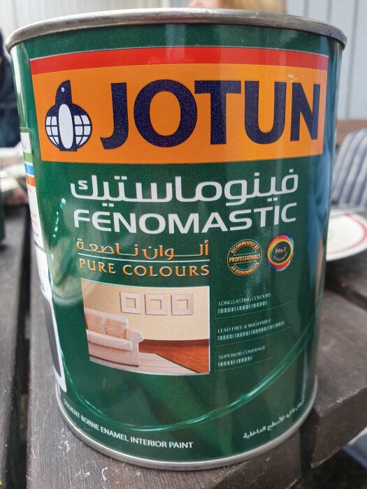 Burk med Jotun Fenomastic färg, grönt med text och logotyper, visar interiörbild.
