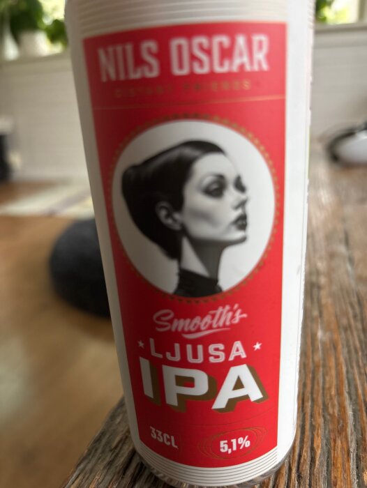 Flaska med etikett från Nils Oscar ljusa IPA, 33 cl, 5,1% alkoholhalt, med stiliserad illustration av en person.