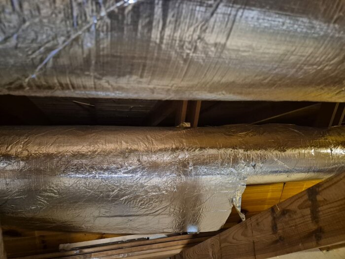 Isolerade ventilationsrör i taket på en vind, omgivna av träbjälkar och takpaneler.