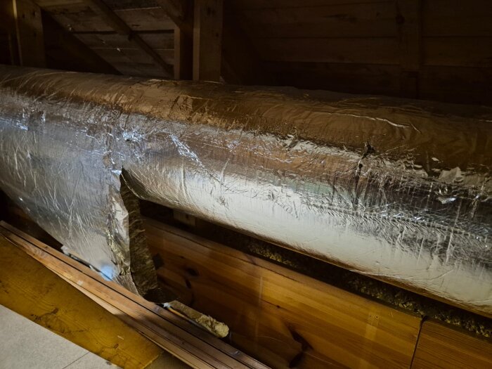 Isolerad ventilationskanal på vind med synlig skada i folien.