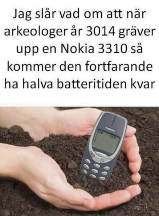 En person håller en Nokia 3310-telefon i händerna, halvt täckt av jord, tillsammans med en humoristisk text om framtida batteritid.