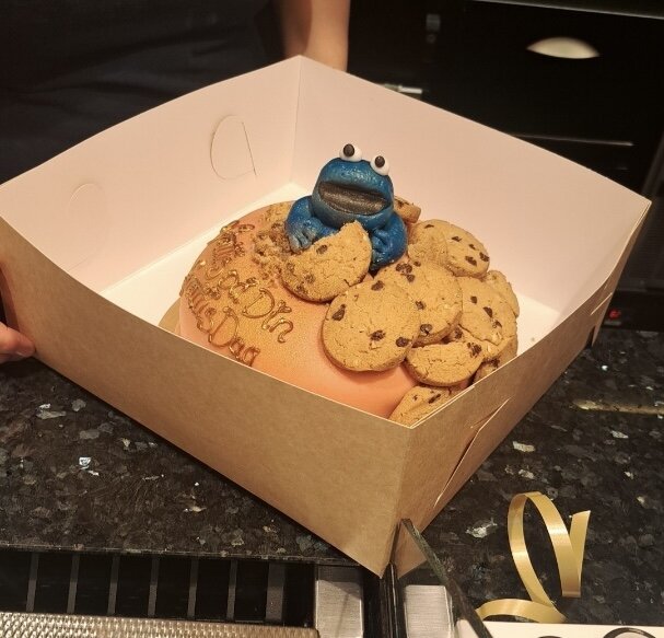 Tårta med blå figur och chokladkakor på toppen, dekorerad för ett 1-årsdagfirande, i en kartonglåda.