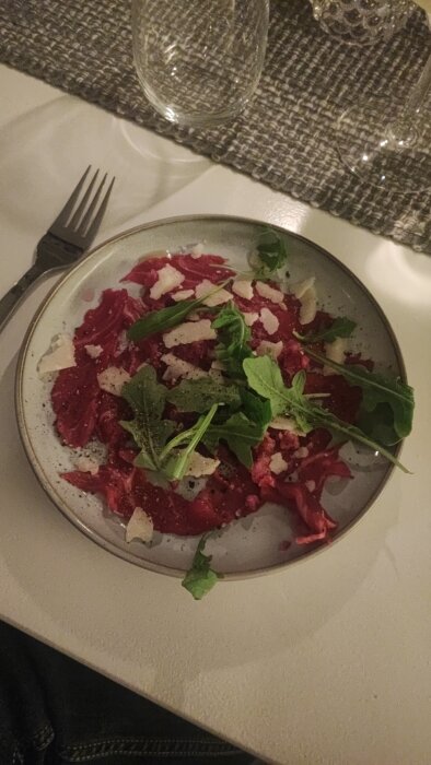 Tallrik med carpaccio, parmesan och ruccola på dukat bord.