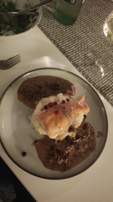 Tallrik med ugnsbakad lax på potatispuré, täckt av trattkantarellsås och dekorerad med picklade lingon.