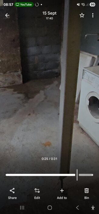 Fuktfläck på golv nära tegelvägg och tvättmaskin, potentiellt läckage, med mörka områden som kan indikera vattenskada vid rör.